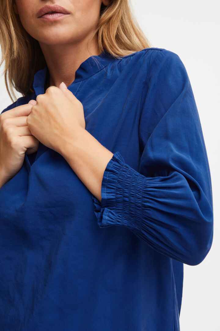The Charlene is a blouse for those who just want something plain coloured yet stylish to update their wardrobe.  This useful staple comes in a beautiful cobalt or "sodalite" blue or cloud white.  It is the shape du jour - colourless, v necked, long full sleeves with ruched deep elasticated cuffs. Plain but pretty at the same time  80% Modal; 20% Polyester  30 degree machine washable   