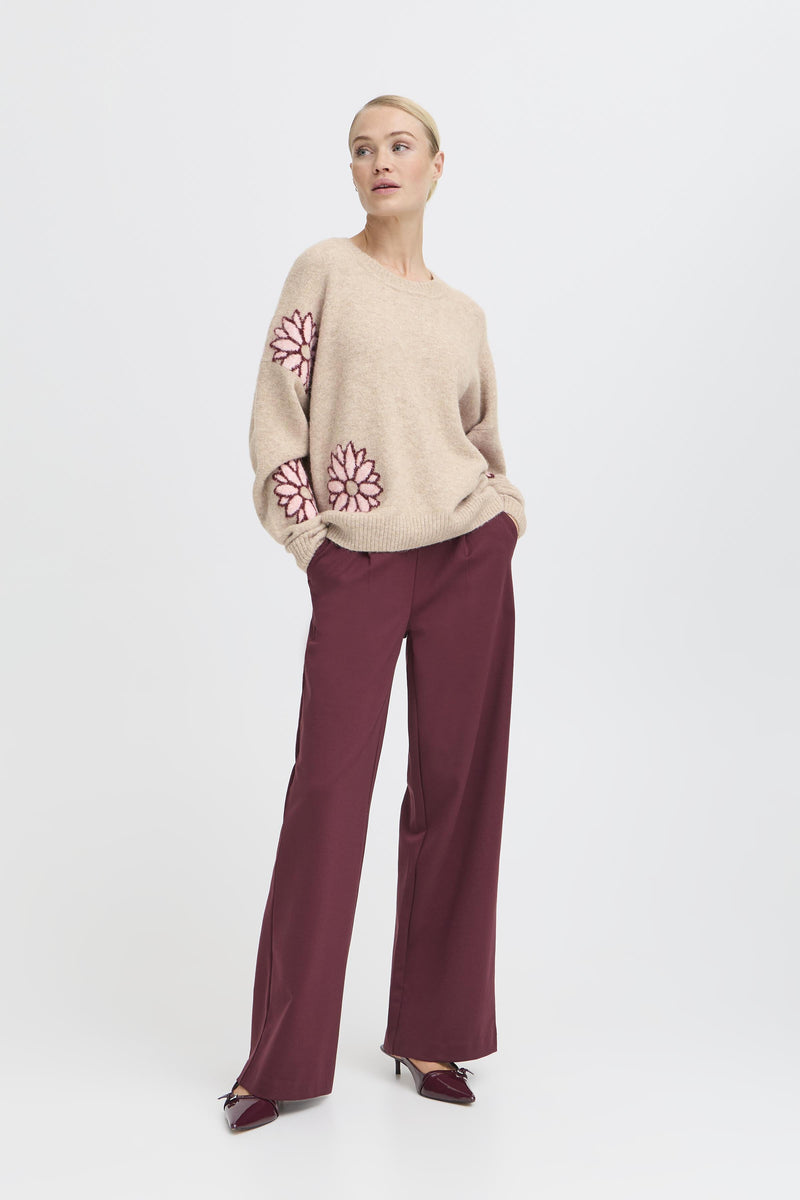 Woman wearing BY Omea sweater with floral patterns and burgundy pants on a white background