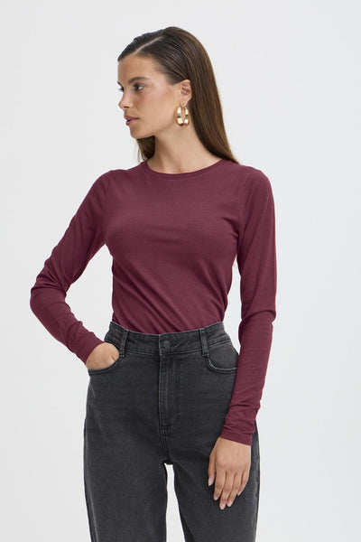 Woman wearing a maroon long-sleeve top and black jeans on a white background