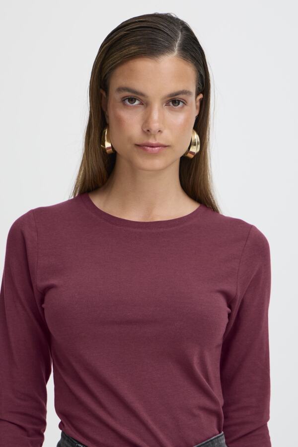Woman wearing a maroon long-sleeve top against a plain background