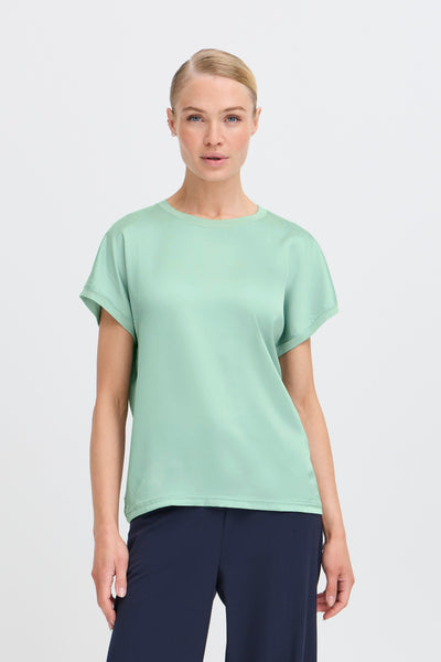 Woman wearing a light green t-shirt and dark pants on a white background