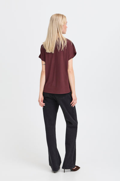 Woman wearing a burgundy top and black pants on a white background showing the rear