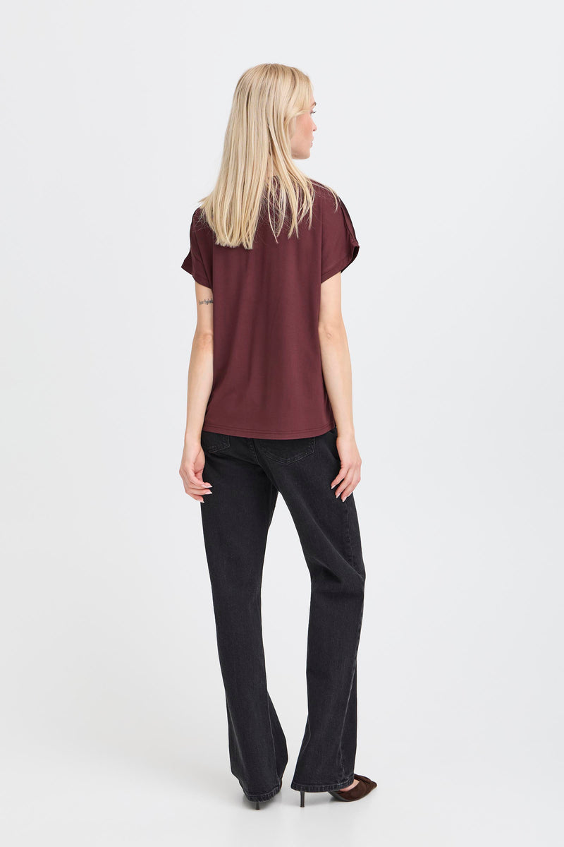 Woman wearing a burgundy top and black pants on a white background showing the rear