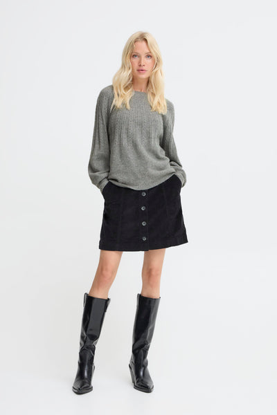 Woman wearing a gray sweater, black skirt, and black knee-high boots on a white background