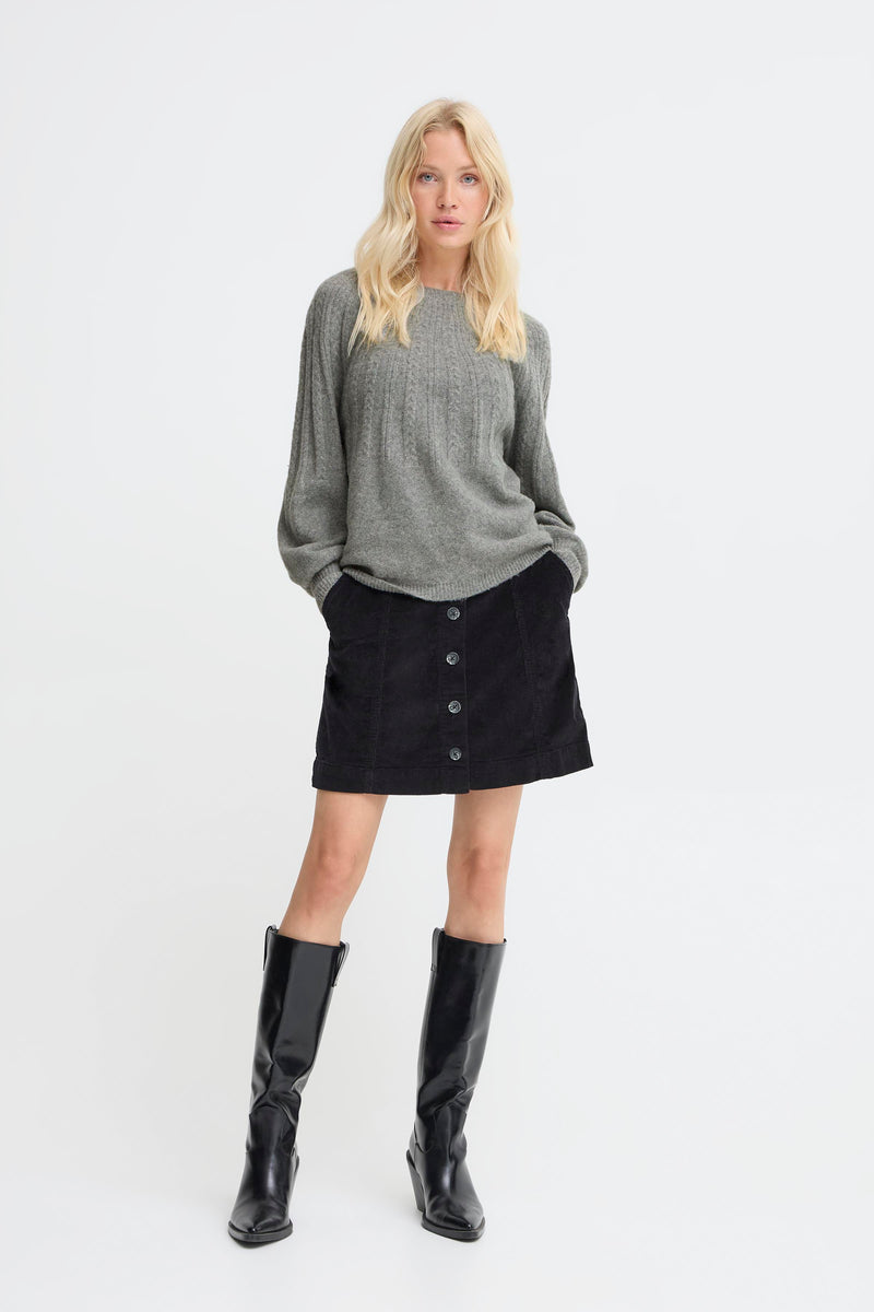 Woman wearing a gray sweater, black skirt, and black knee-high boots on a white background