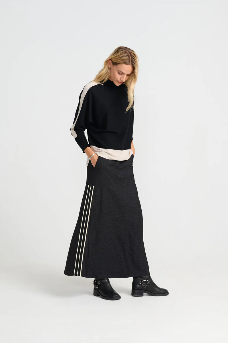 Woman wearing a costamani black jumper with white stripes on sleeves over a long black skirt 