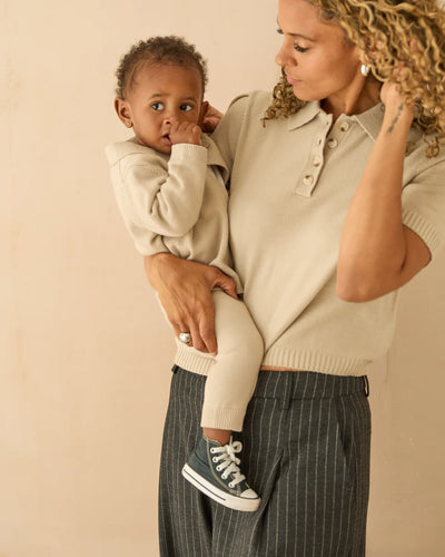 Woman holding a child wearing a beige sweater against a beige background