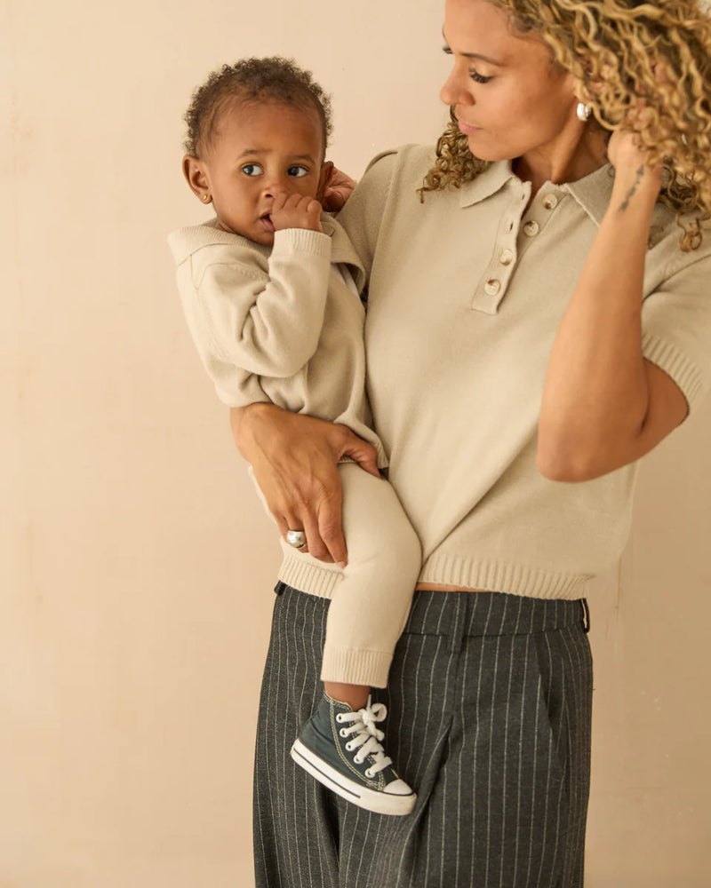 Woman holding a child wearing a beige sweater against a beige background