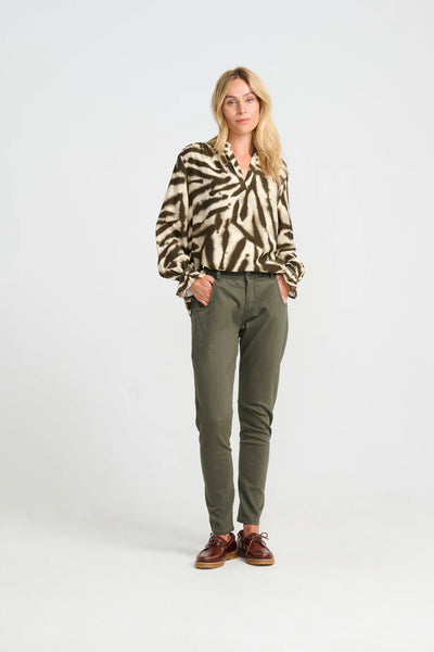Woman wearing a patterned shirt and green pants on a white background