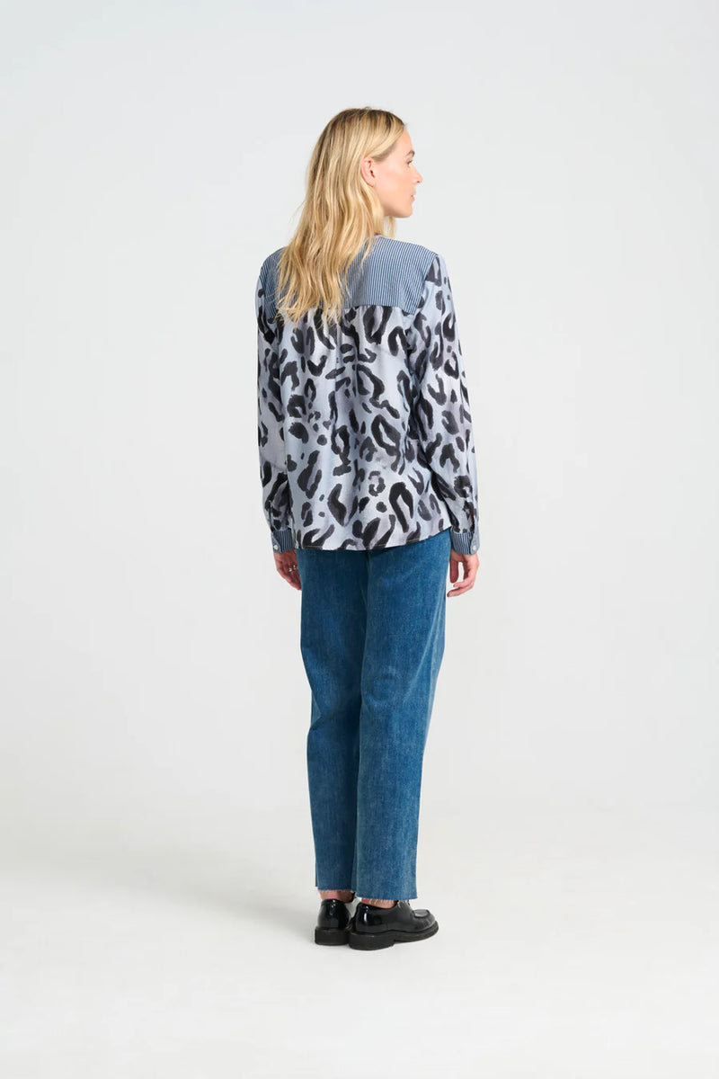 Woman wearing a patterned shirt and blue jeans on a white background