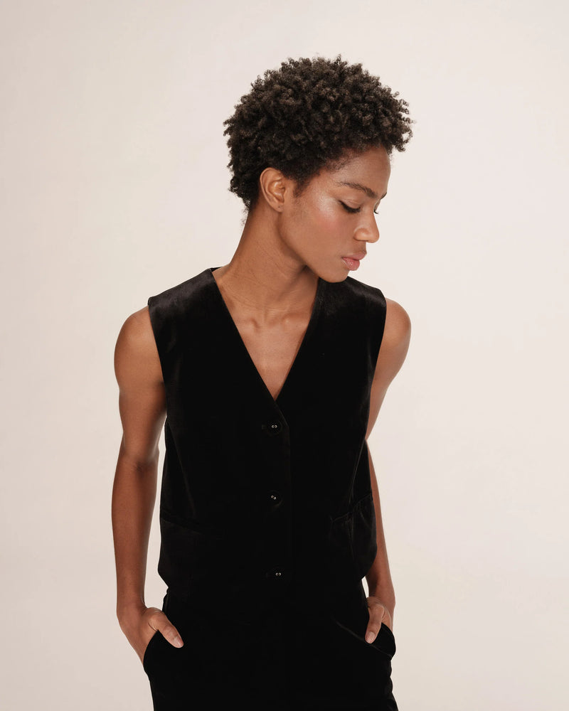 Person wearing a black velbet v neck waistcoat against a plain background