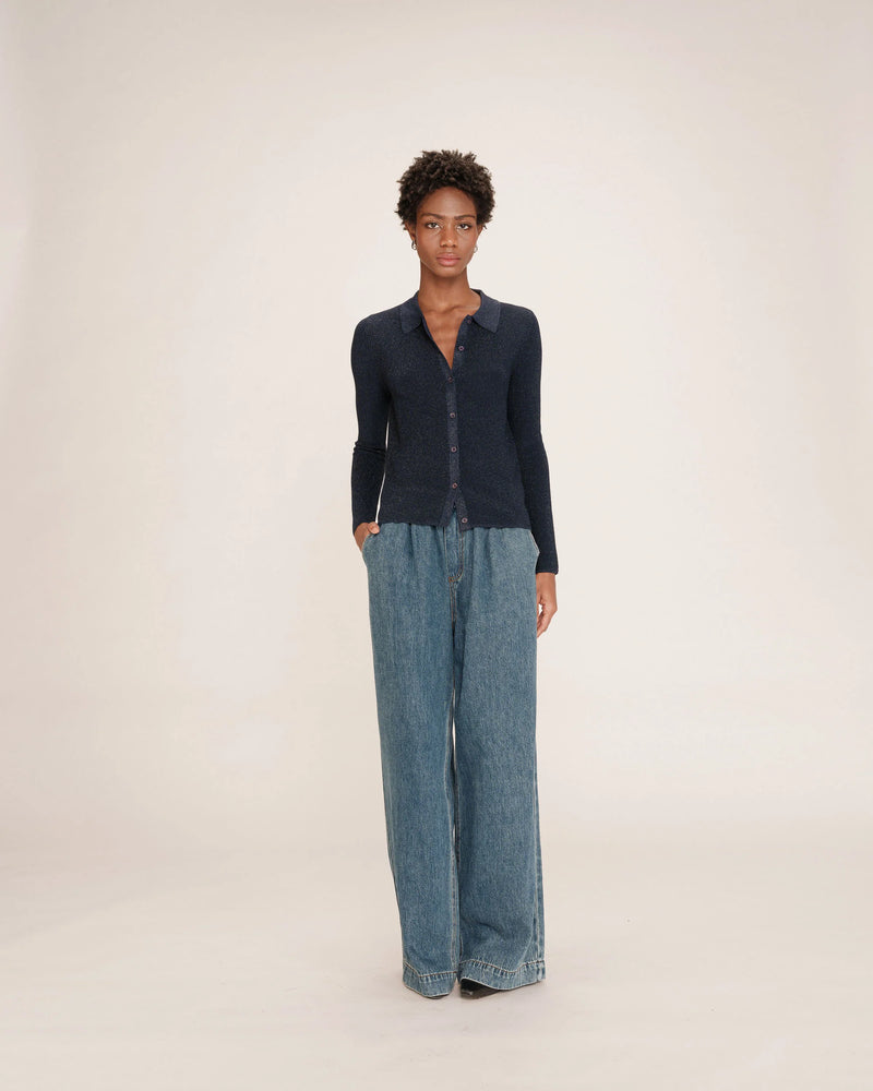 Person wearing a dark blue lurex cardigan and wide-leg jeans on a white background