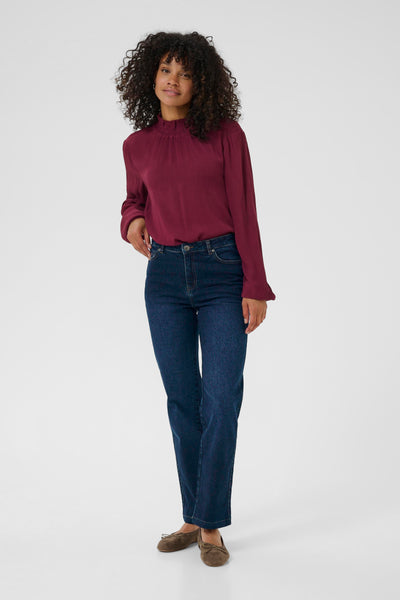 Woman wearing a burgundy top and blue jeans on a white background