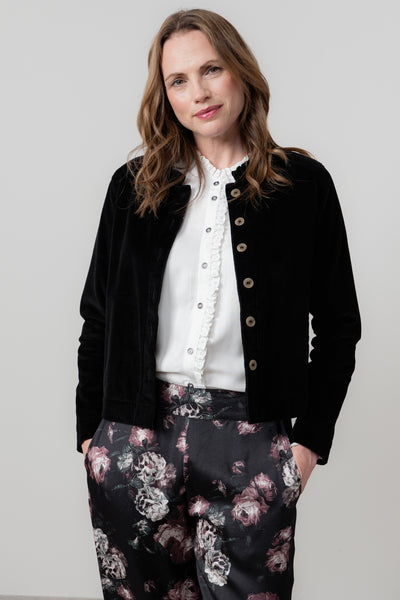 Woman wearing lily & me black jacket, white blouse, and floral pants against a plain background