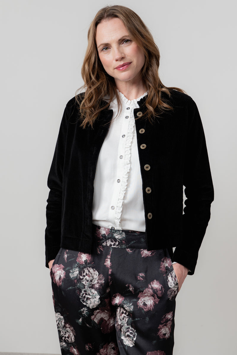 Woman wearing lily & me black jacket, white blouse, and floral pants against a plain background