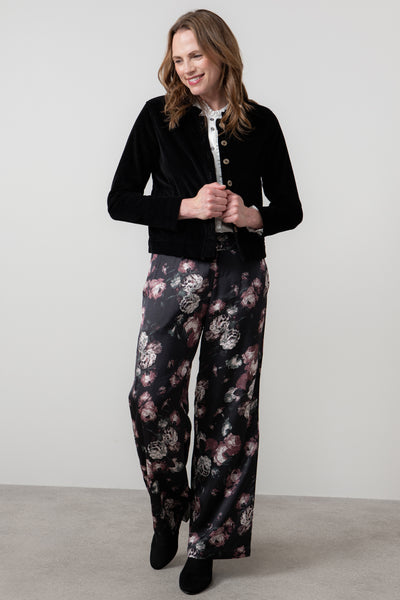 Woman wearing rene black jacket and floral pants on a plain background