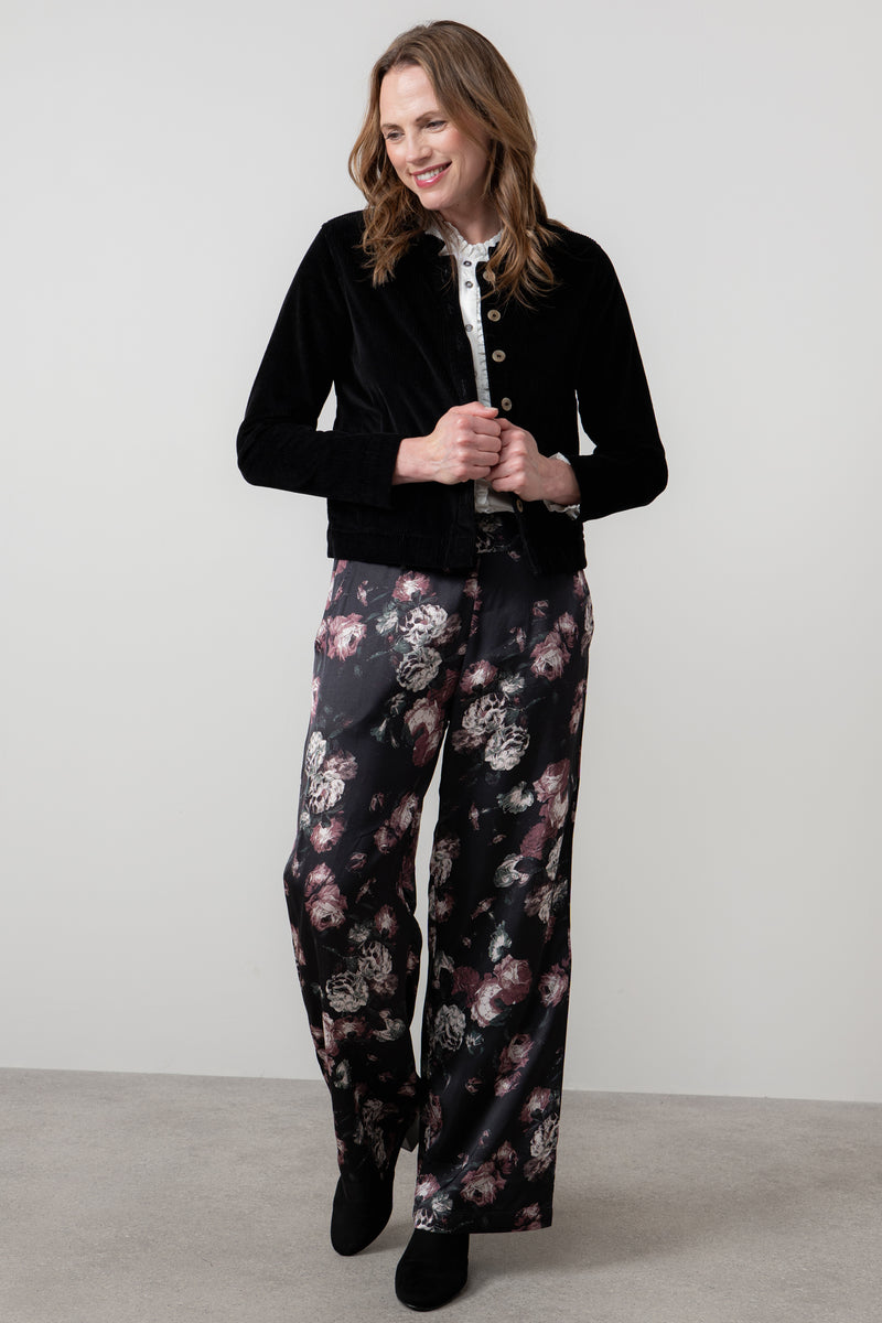Woman wearing rene black jacket and floral pants on a plain background