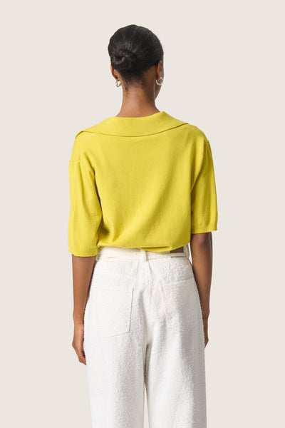 Back view of model wearing Spina Short Sleeve top with collar, worn tucked into white trousers.