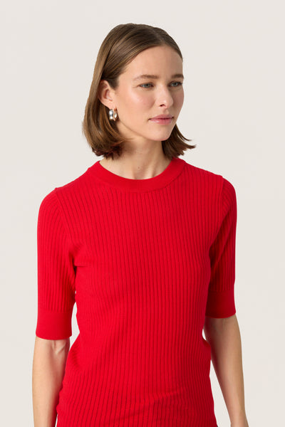 Woman wearing a red ribbed sweater against a plain background