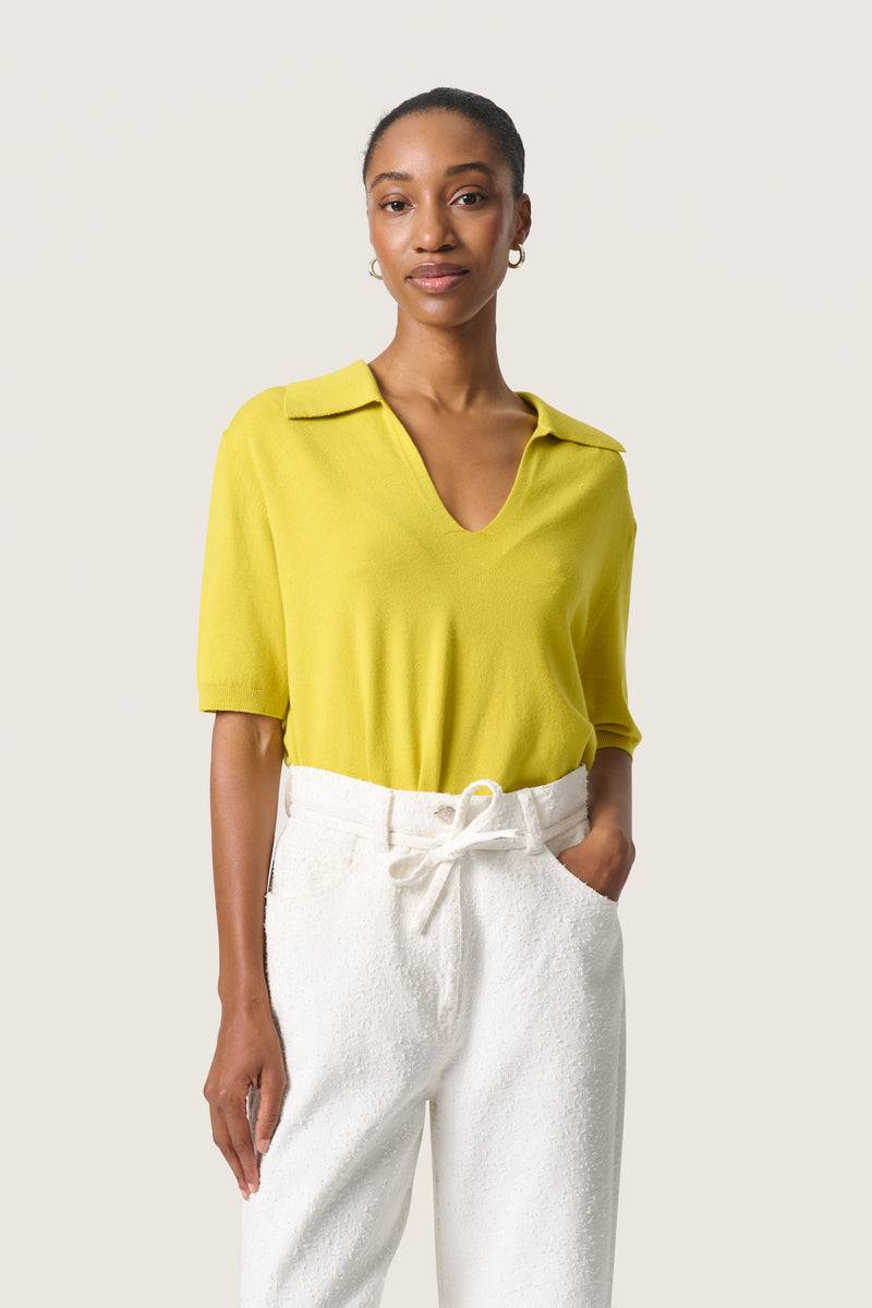 Front view of model wearing Spina Short Sleeve top with open collar tucked into white trousers.