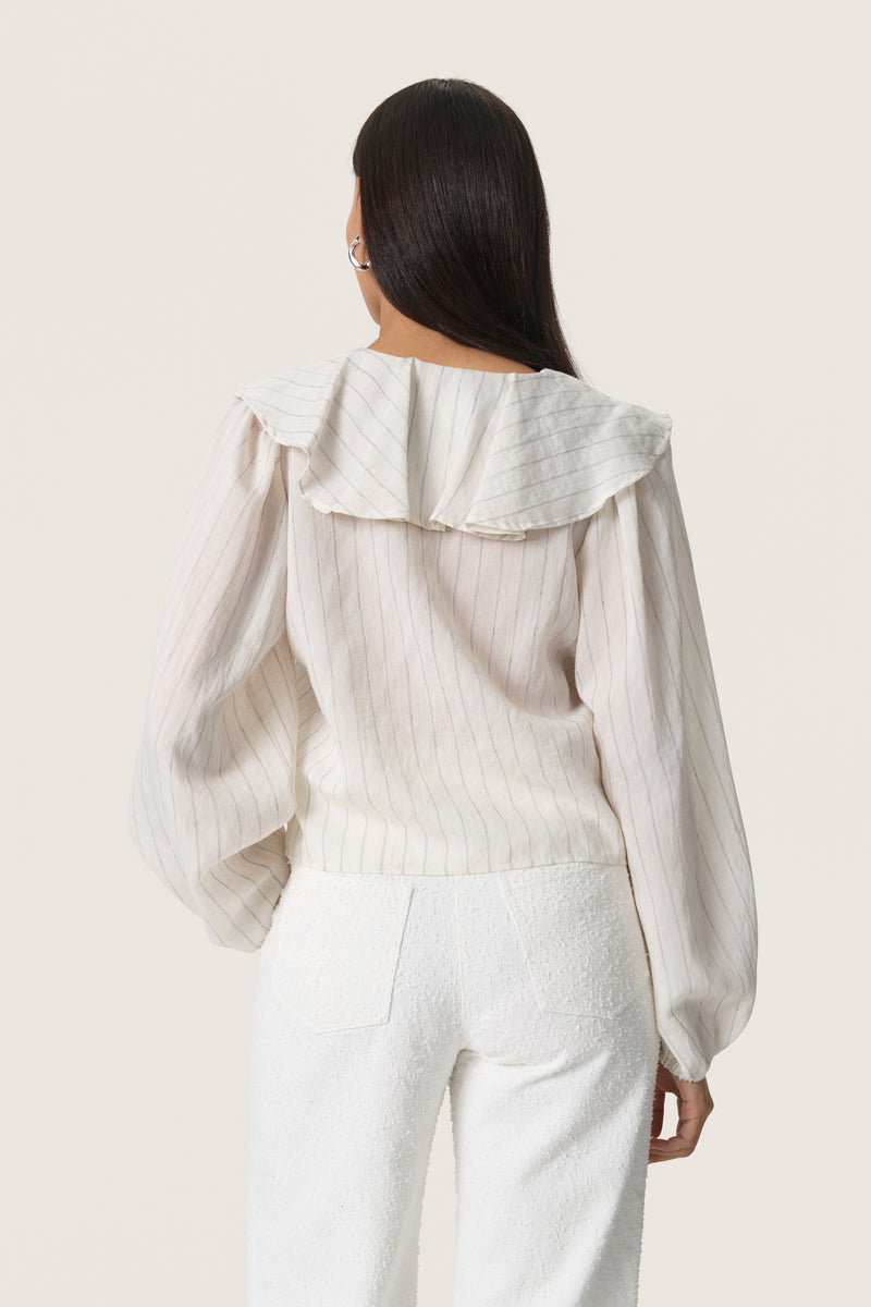 back view of model wearing soaked in luxury roya cream blouse with fine dark stripe, soft ruffled v neck collar and long sleeves