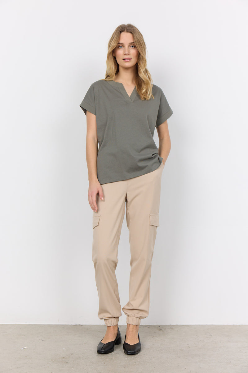 Front full view of Soyaconcept Short Sleeve sage green top with tailored v neck. Shown worn loose with beige trousers