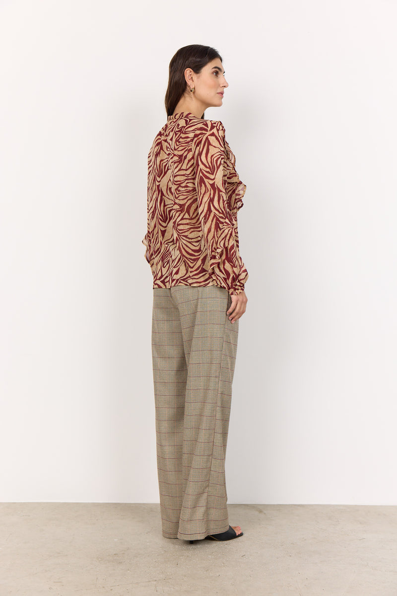 Woman wearing a patterned shirt and plaid pants against a white background