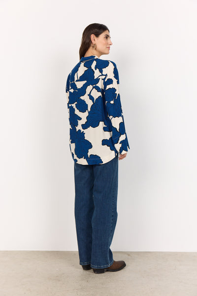 Woman wearing a blue and white patterned shirt with blue jeans on a white background