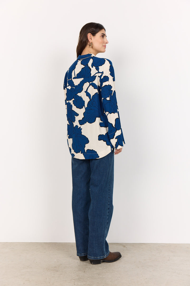 Woman wearing a blue and white patterned shirt with blue jeans on a white background