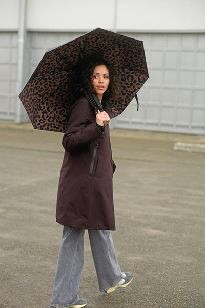 Person holding a leopard print umbrella and wearing Yest Zina brown coat in an urban setting
