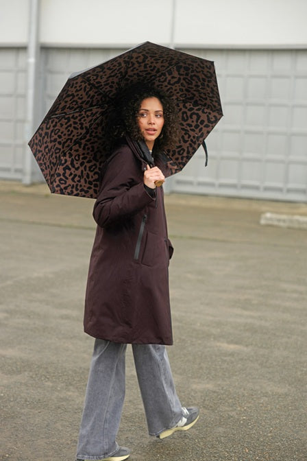 Person holding a leopard print umbrella and wearing Yest Zina brown coat in an urban setting