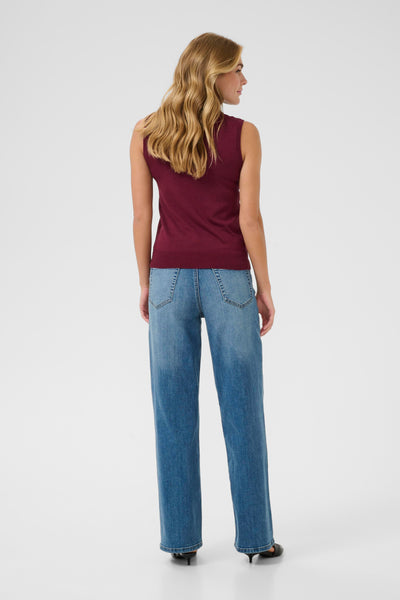 Woman wearing kaffe sleeveless burgundy top and blue jeans on a white background