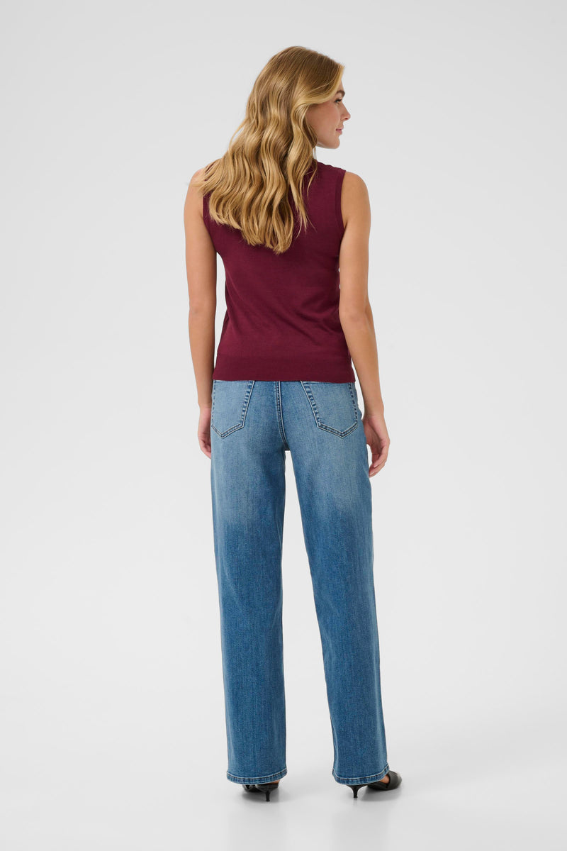 Woman wearing kaffe sleeveless burgundy top and blue jeans on a white background