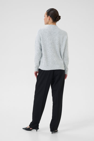 Person wearing a light gray sweater and black pants on a white background
