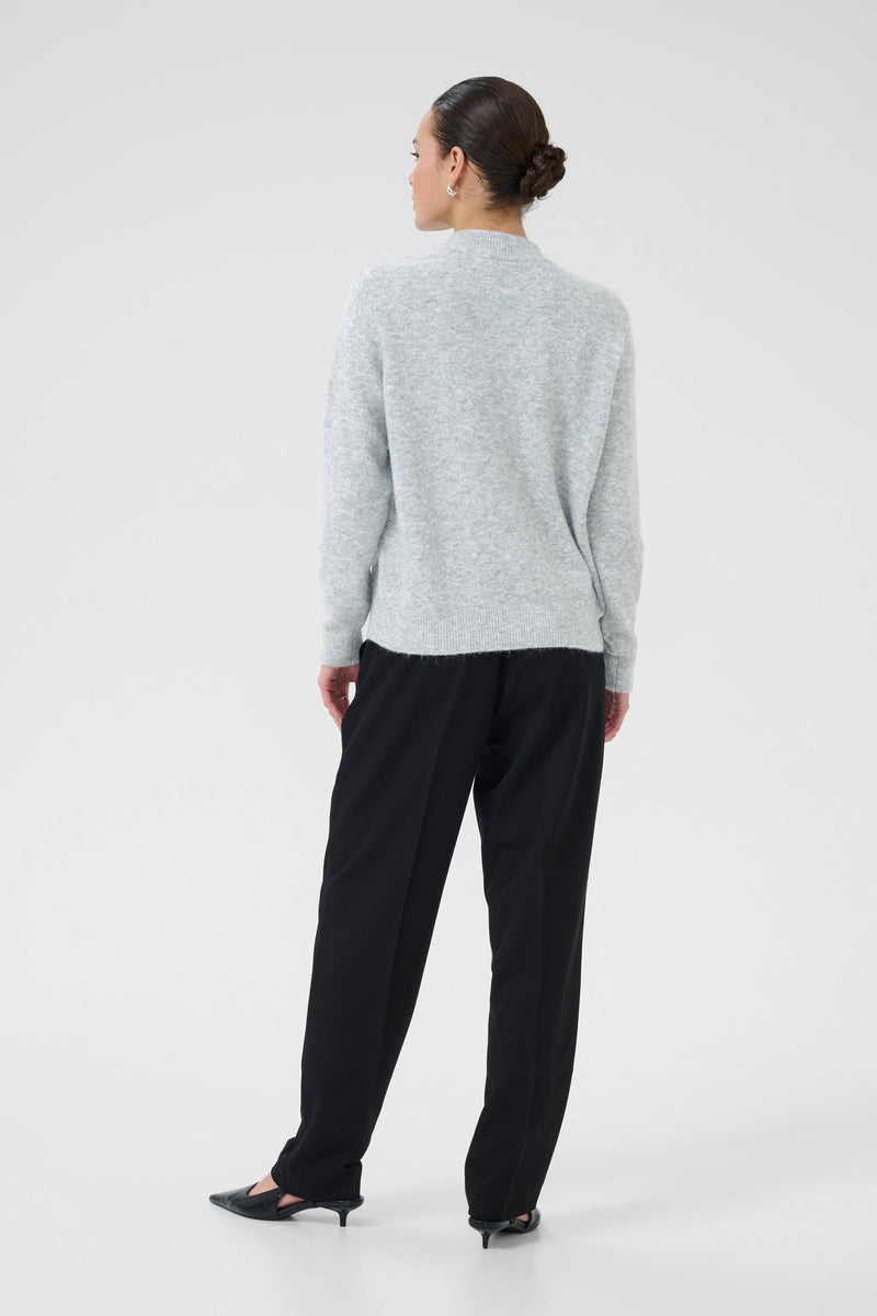 Person wearing a light gray sweater and black pants on a white background