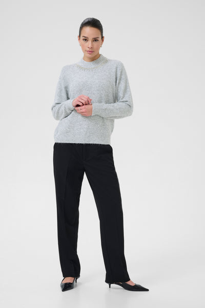 Woman wearing kaffe light gray sweater and black pants on a white background