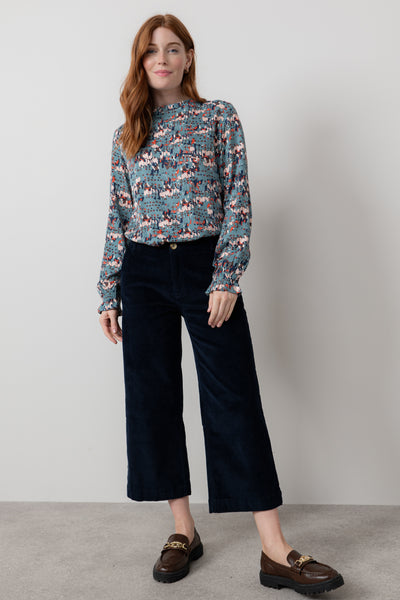 Woman wearing a patterned blouse and black pants against a plain background