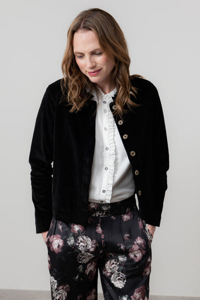 Woman wearing rene black jacket, white blouse, and floral pants against a plain background