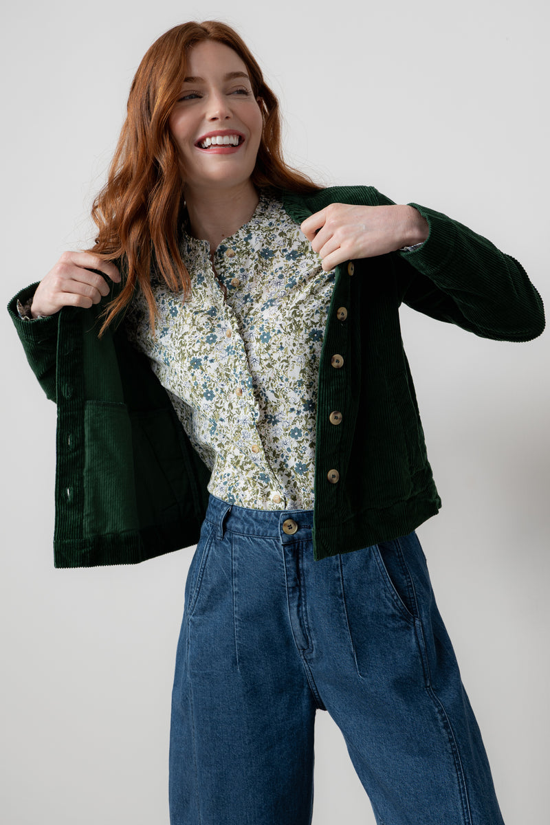 Woman wearing rene green jacket over a floral shirt and blue jeans on a white background