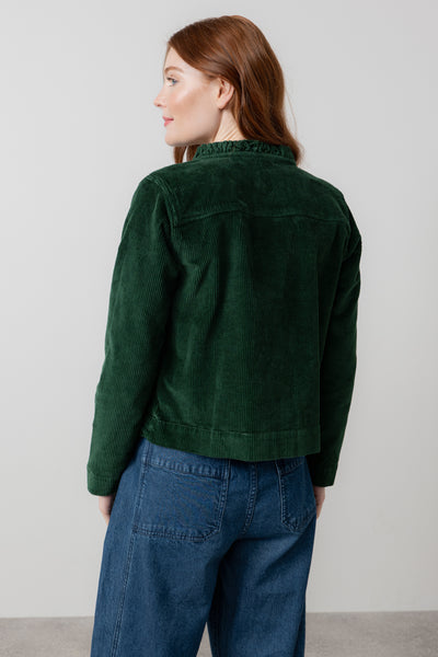 Person wearing green rene jacket and blue jeans against a plain background