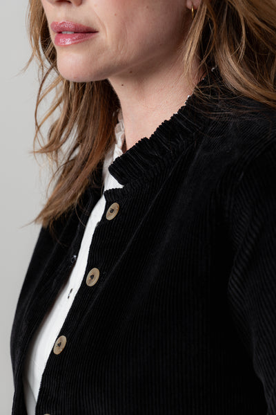 Close-up of a person wearing lily & me black jacket with button details on a plain background