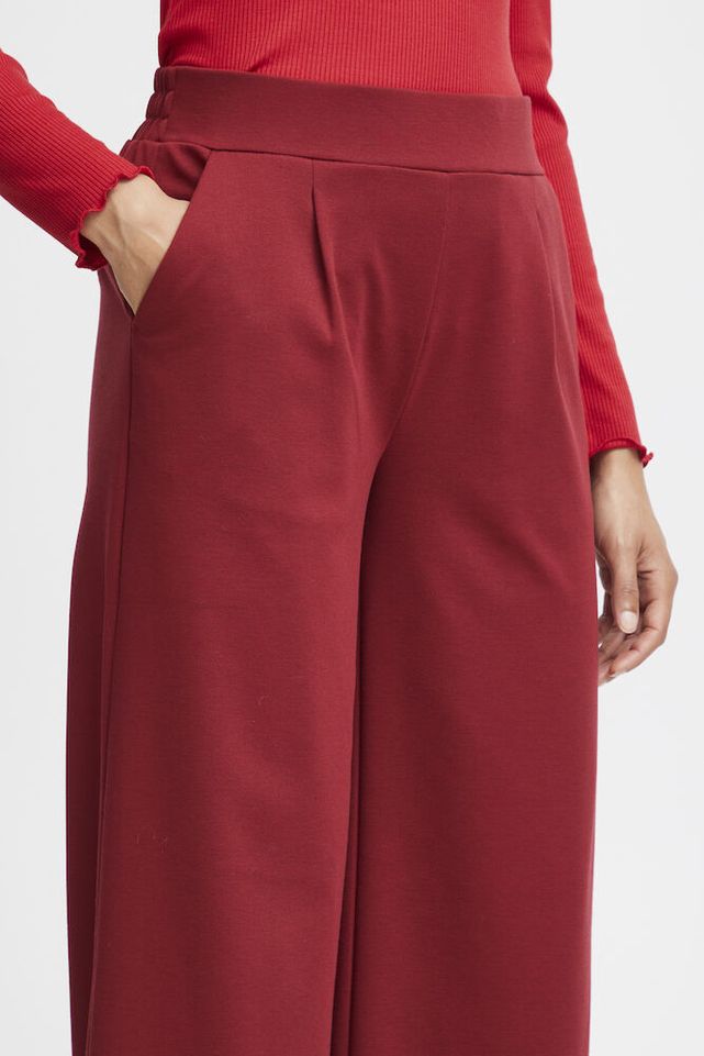 Burgundy pants worn with a red top on a white background