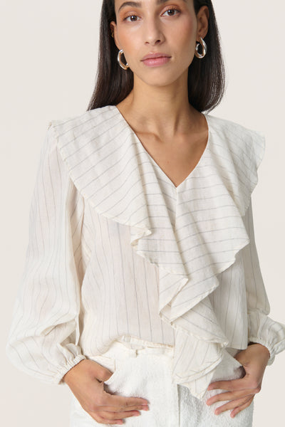 close up of model wearing soaked in luxury roya cream blouse with fine dark stripe, soft ruffled v neck collar and long sleeves 